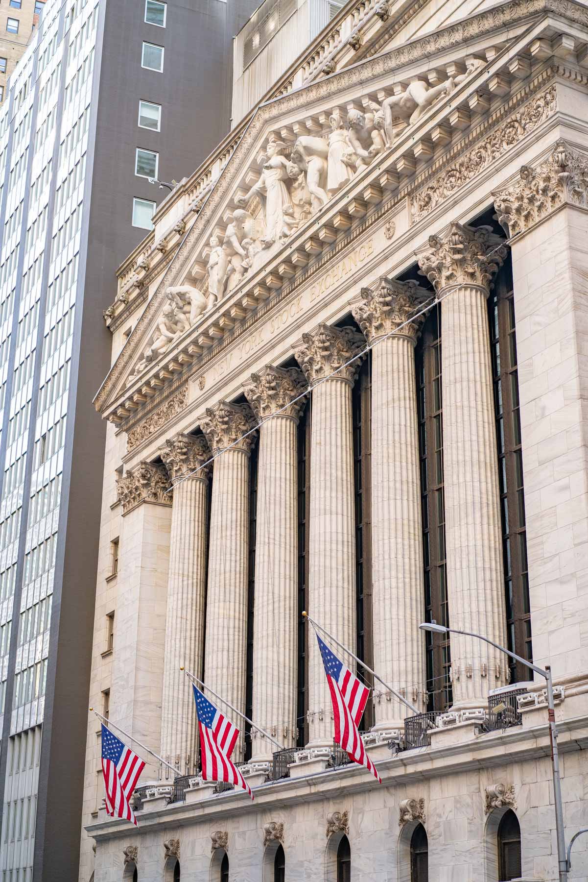 The neoclassical facade of the New York Stock Exchange with American flags on Wall Street.