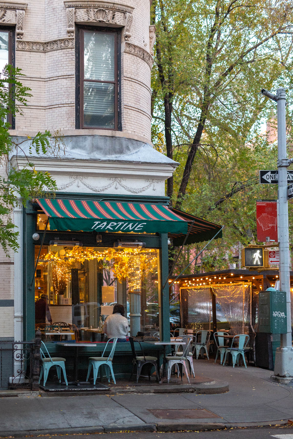 Empty chairs and tables are setup outside Tartine in the West Village. Twinkly lights strung both indoors and in the outdoor seating patio