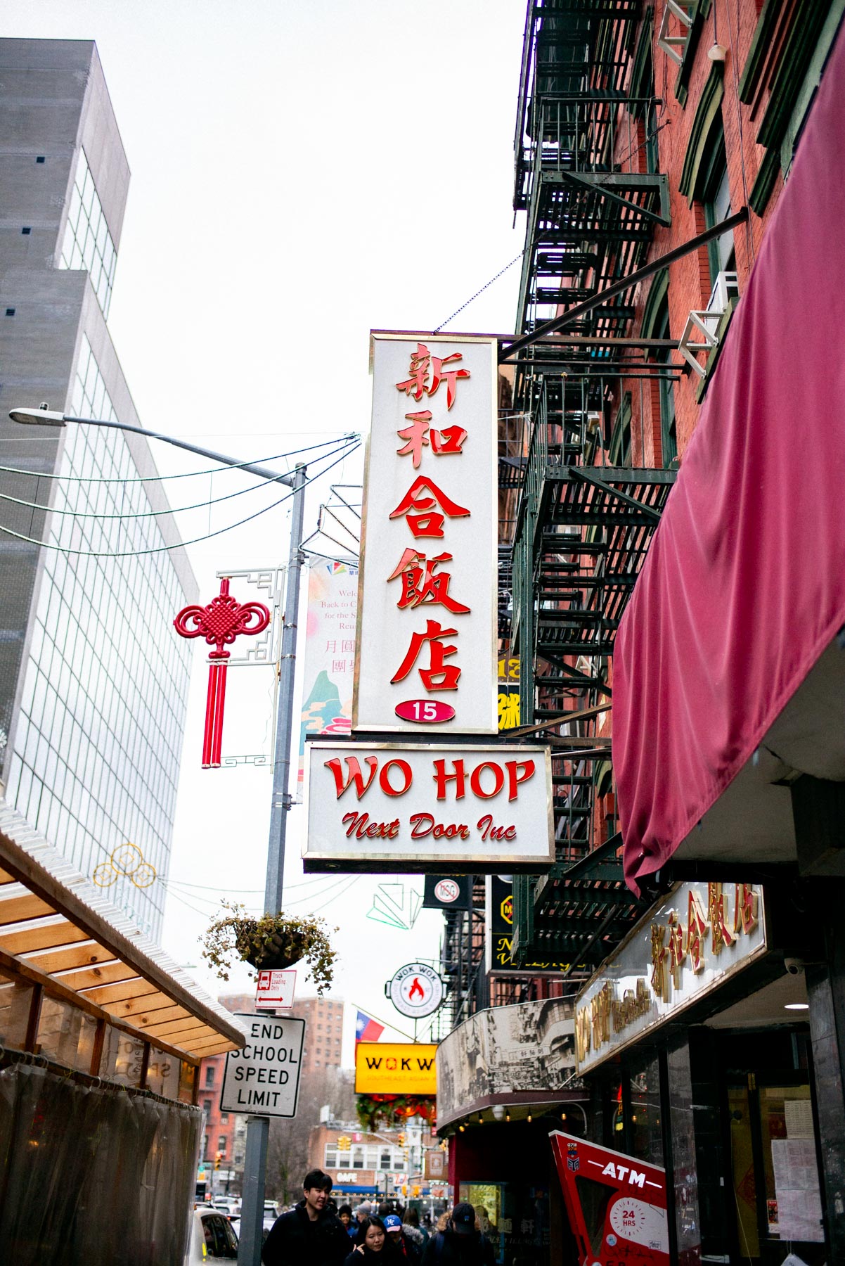 A vertical sign for Wo Hop restaurant hangs above a Chinatown street lined with fire escapes and awnings.