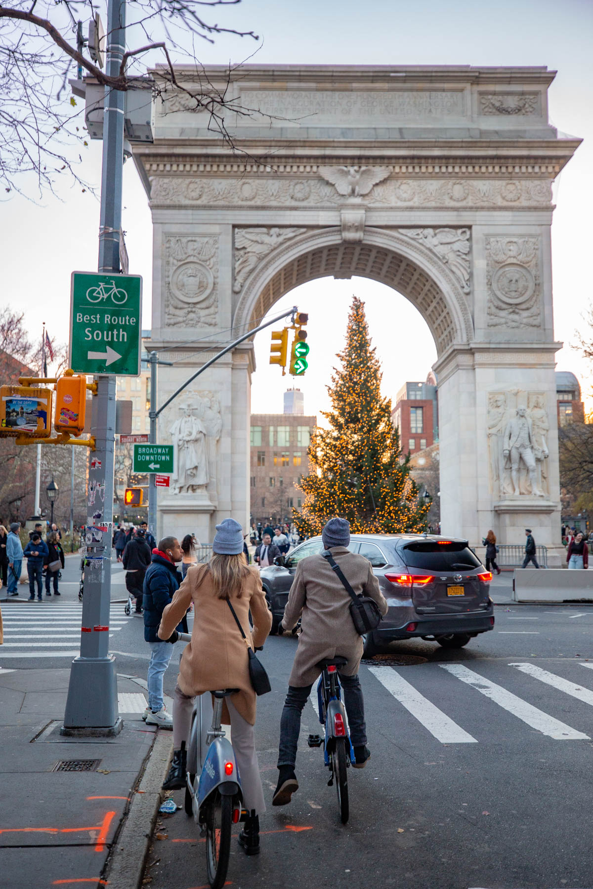 Cyclists ride toward Washington Square Arch with the park's Christmas tree lit inside it.