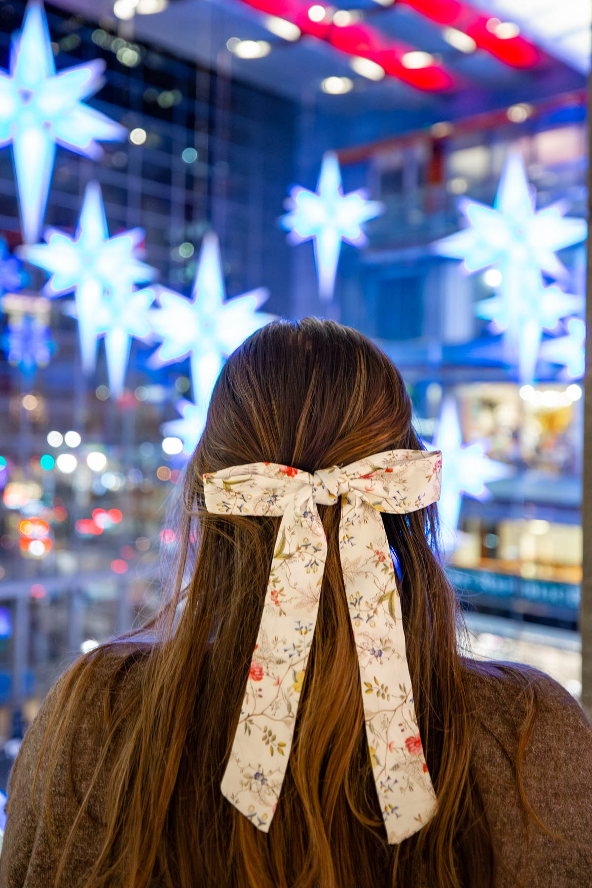 A woman with a floral hair bow faces illuminated star-shaped Christmas lights at Columbus Circle.