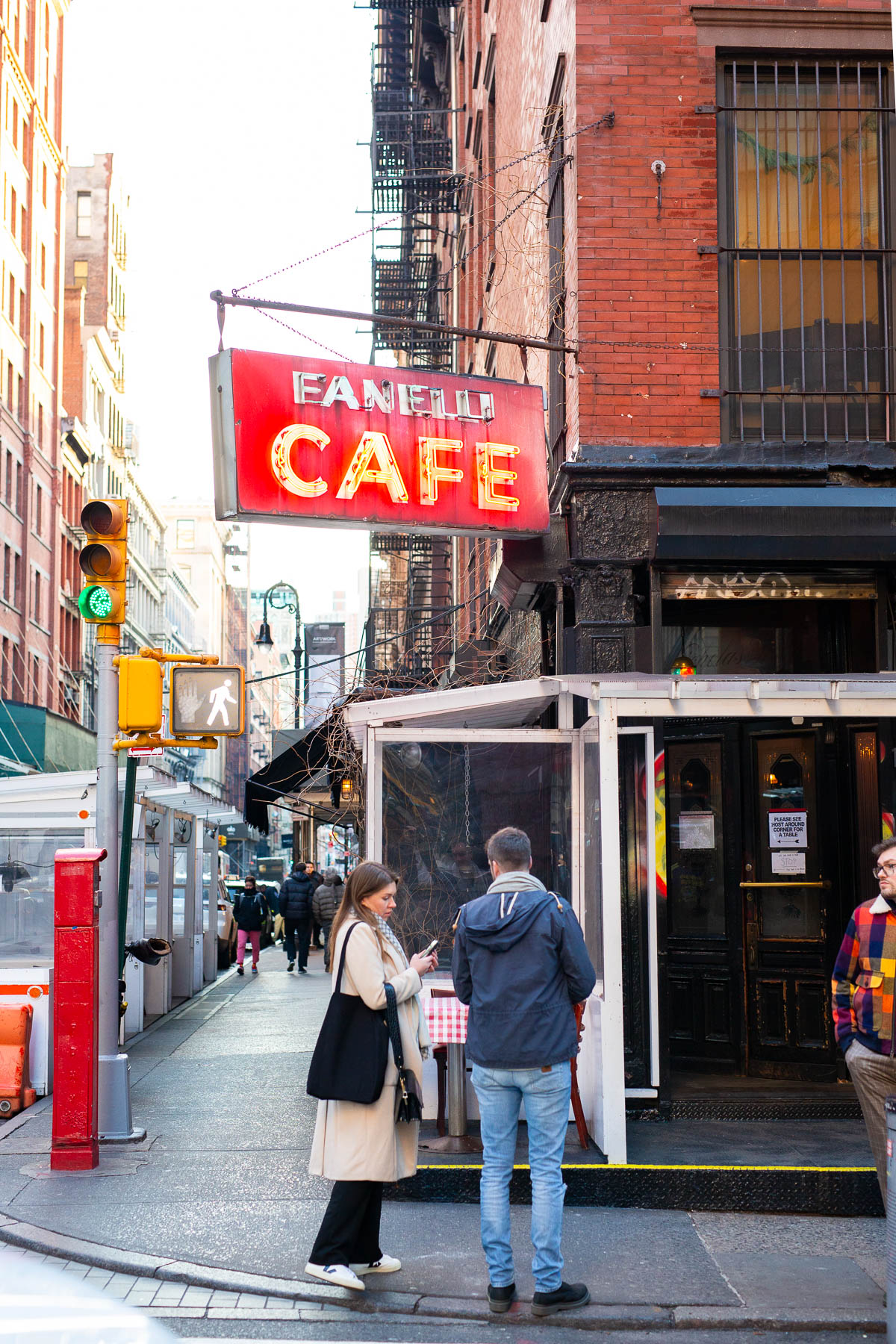 Pedestrians stand on a Soho street corner beneath the red Fanelli Cafe sign.