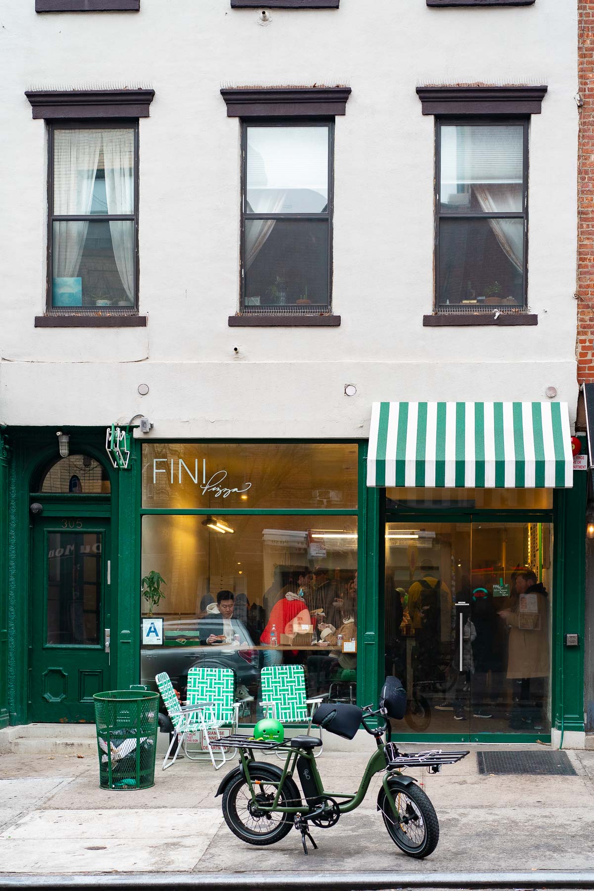 A storefront view of Fini Pizza with a green striped awning and a bicycle parked outside