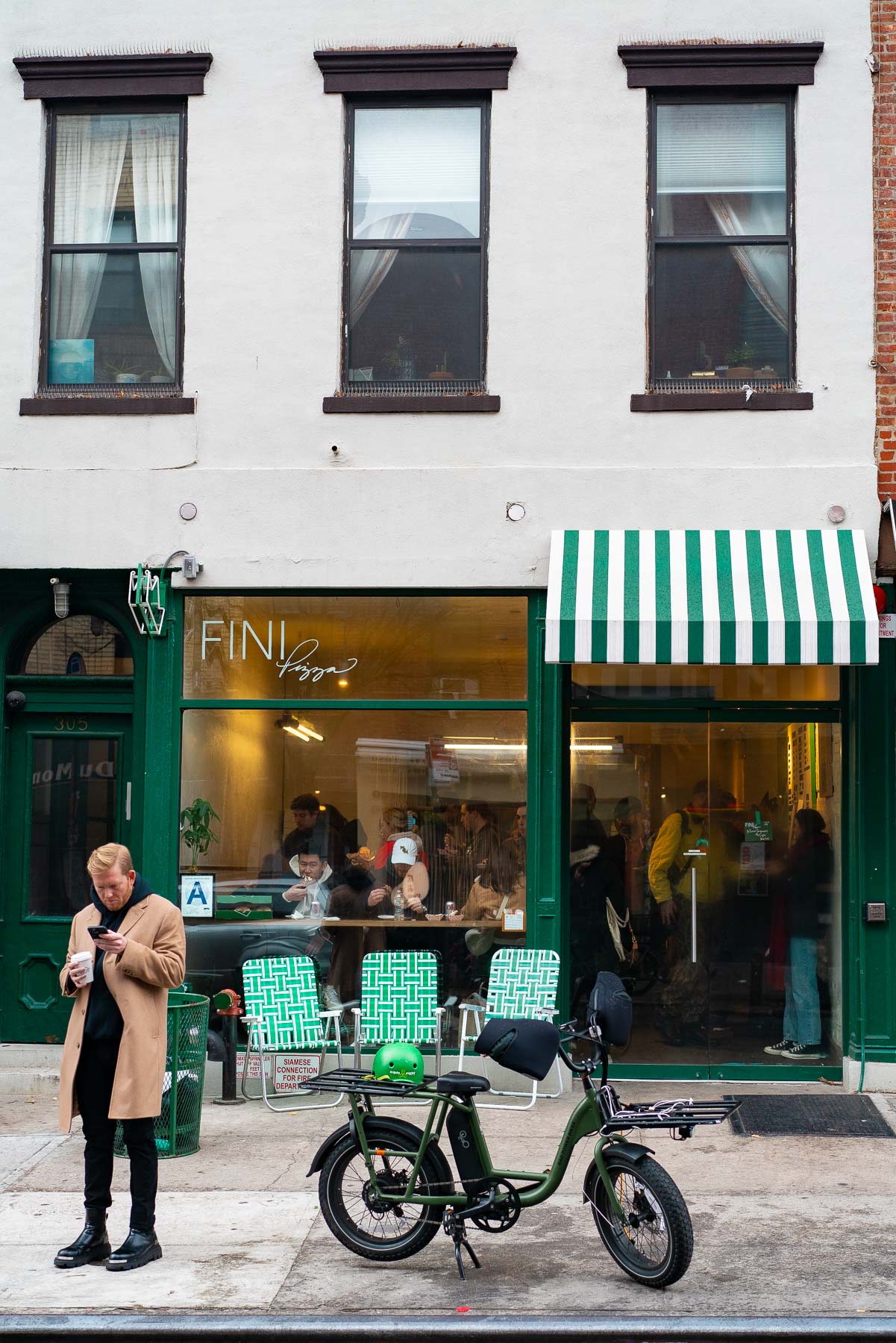 A man checks his phone outside Fini Pizza in Williamsburg with an e-bike parked at the curb