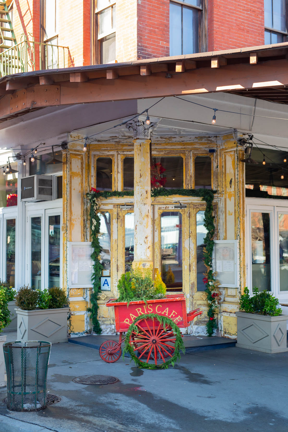A weathered yellow storefront entrance of Paris Cafe decorated with holiday garland in the Financial District.
