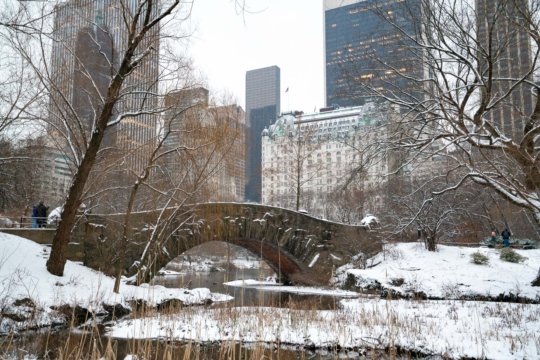 Snow covers Gapstow Bridge and the pond in Central Park with the Plaza Hotel and skyline behind