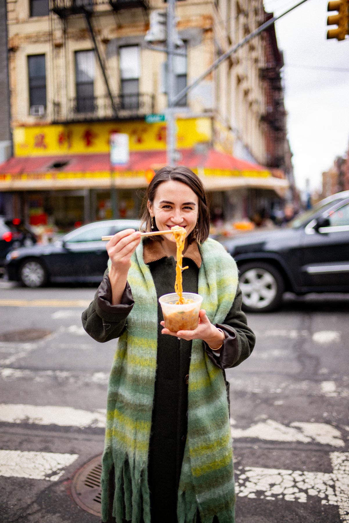 A takeout cup of chili-oil noodles held on a New York City street corner during a Chinatown food crawl