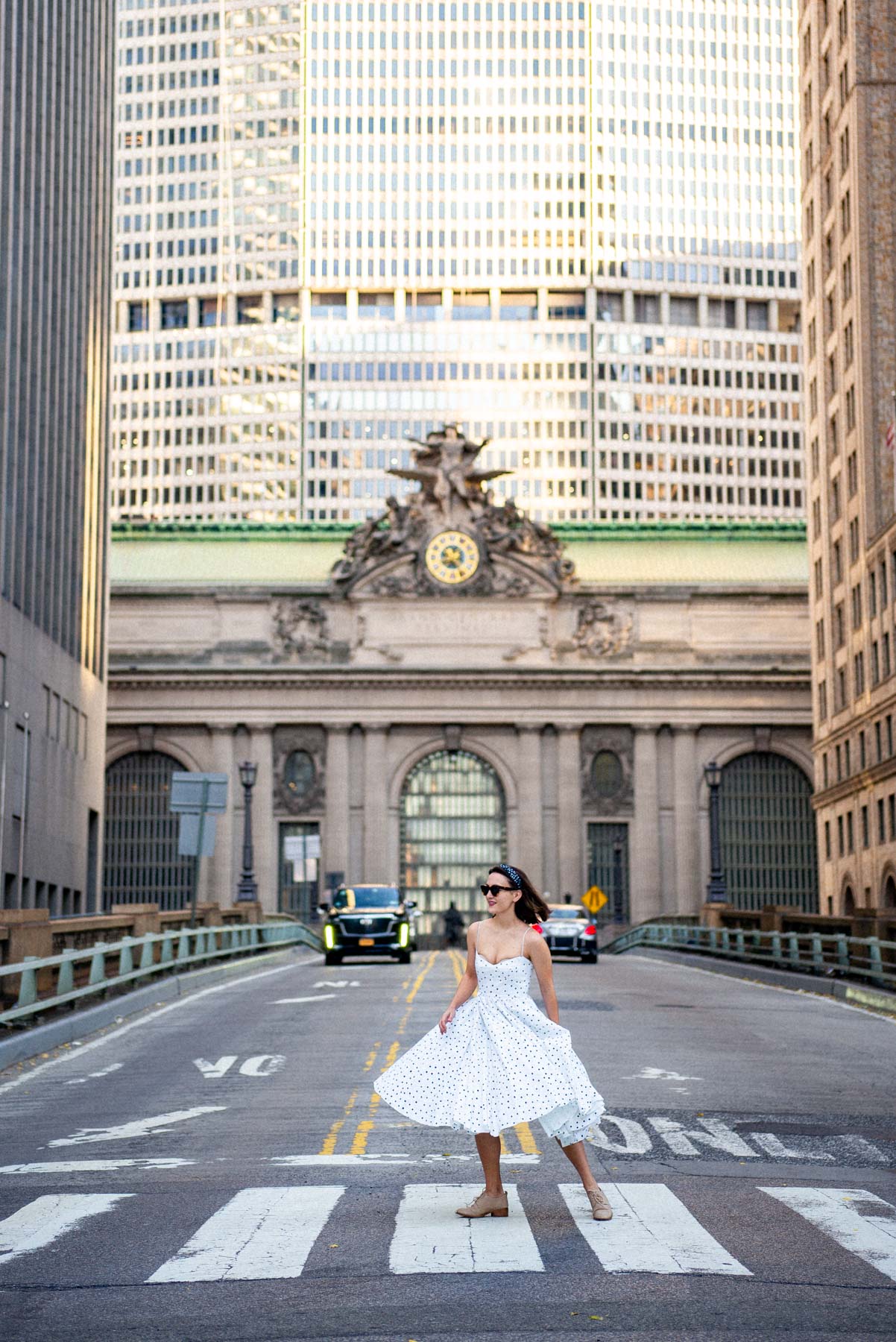 A woman in a polka dot dress twirls on Pershing Square viaduct in front of Grand Central Terminal's facade.