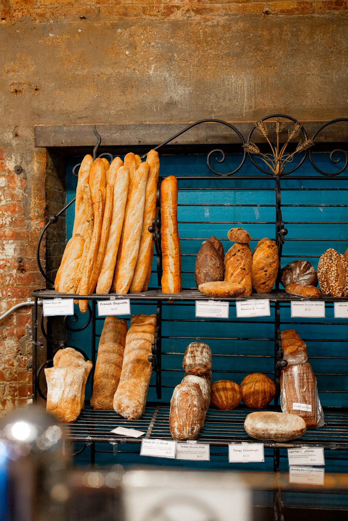 Rustic baguettes and crusty artisan loaves displayed on a black iron rack against exposed brick at a Chelsea Market bakery
