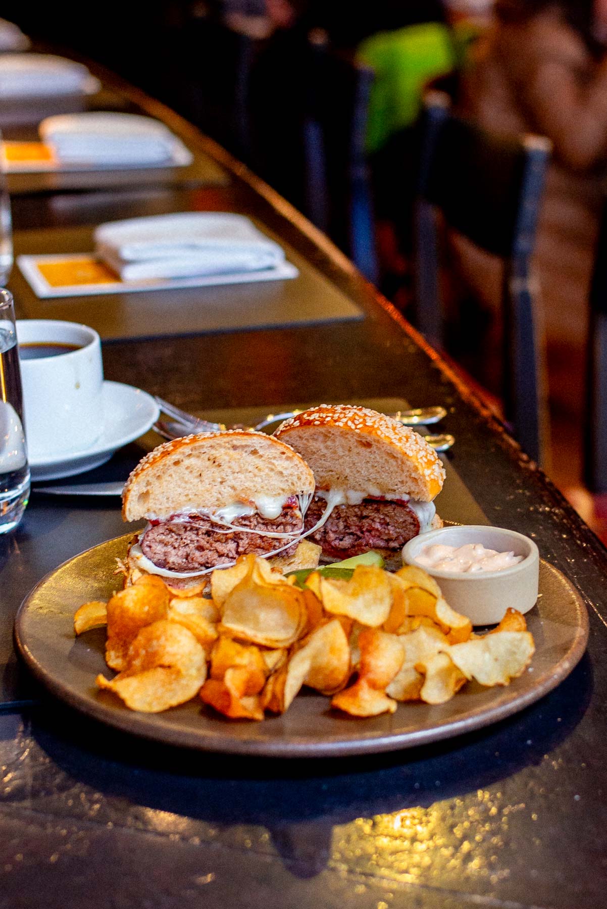 Juicy cheeseburger cut in half with a cheese-pull and chips on a plate at Gramercy Tavern Burger