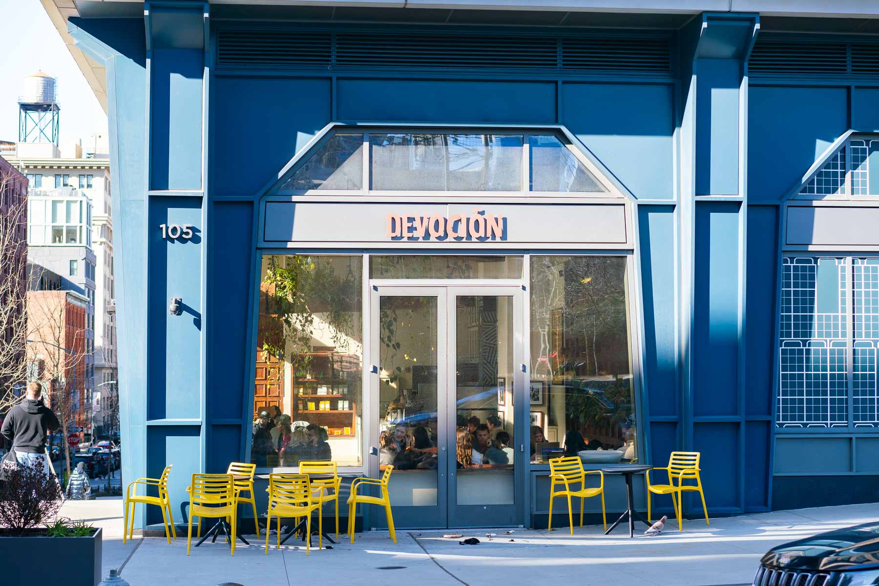The blue storefront of Devoción coffee shop in DUMBO with yellow outdoor chairs.