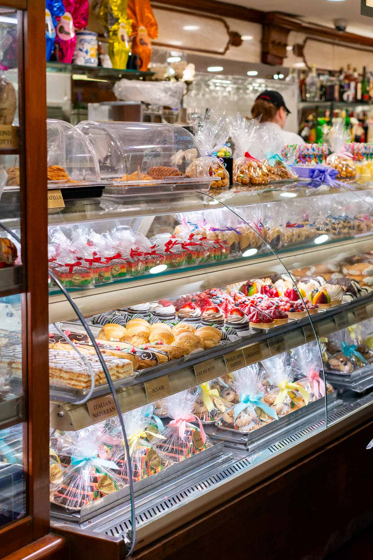 A pastry case at Ferrara Bakery displays Italian desserts wrapped in ribboned cellophane.
