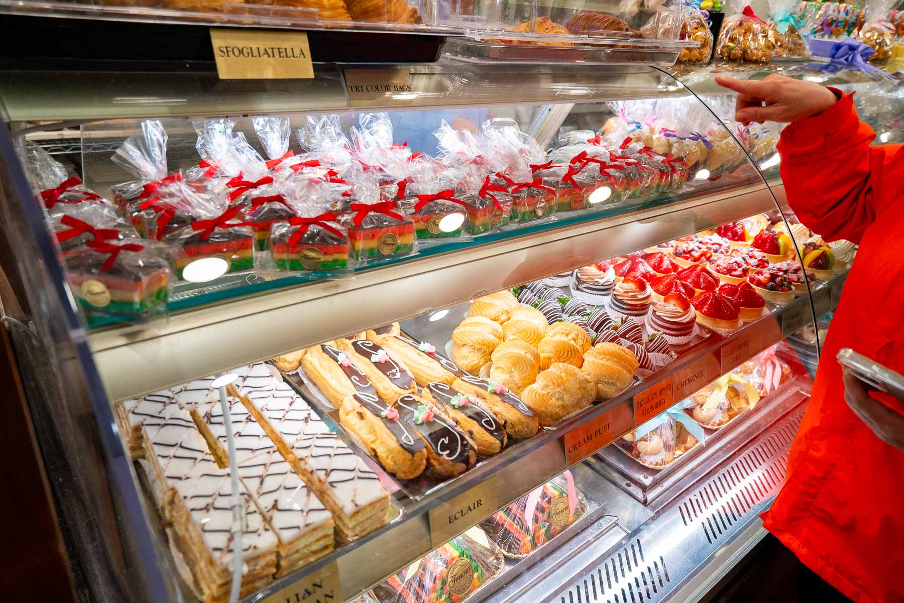 A person points at pastries in a bakery display case at Ferrara Bakery.