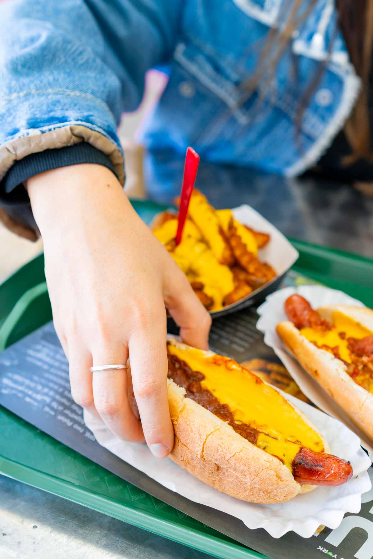 A hand reaches for a chili cheese hot dog on a tray with cheese fries at Nathan's Famous.