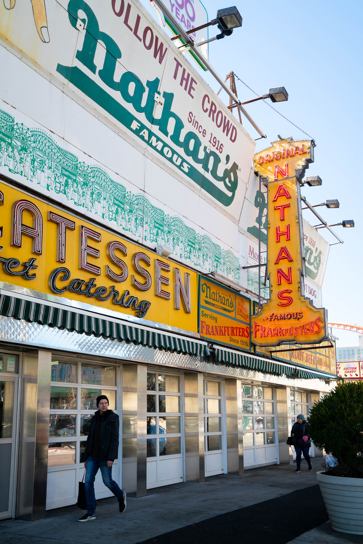 The exterior of Nathan's Famous hot dog stand in Coney Island with signage and a passerby.