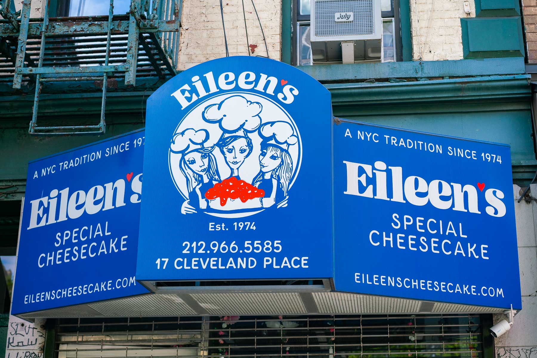 Blue sign with white letters and red accents for Eileen's Special Cheesecake bakery in Soho