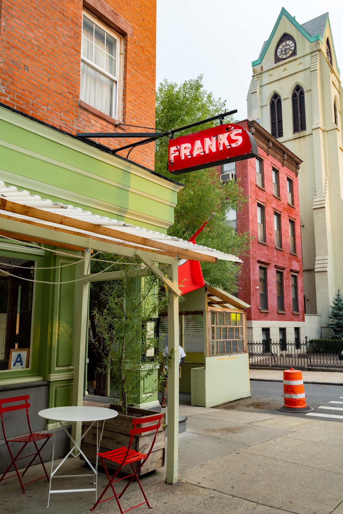 Exterior photo of Frank's Wine Bar's green exterior and red sign with a green patio awning and a metal bistro table set in Carroll Gardens Brooklyn
