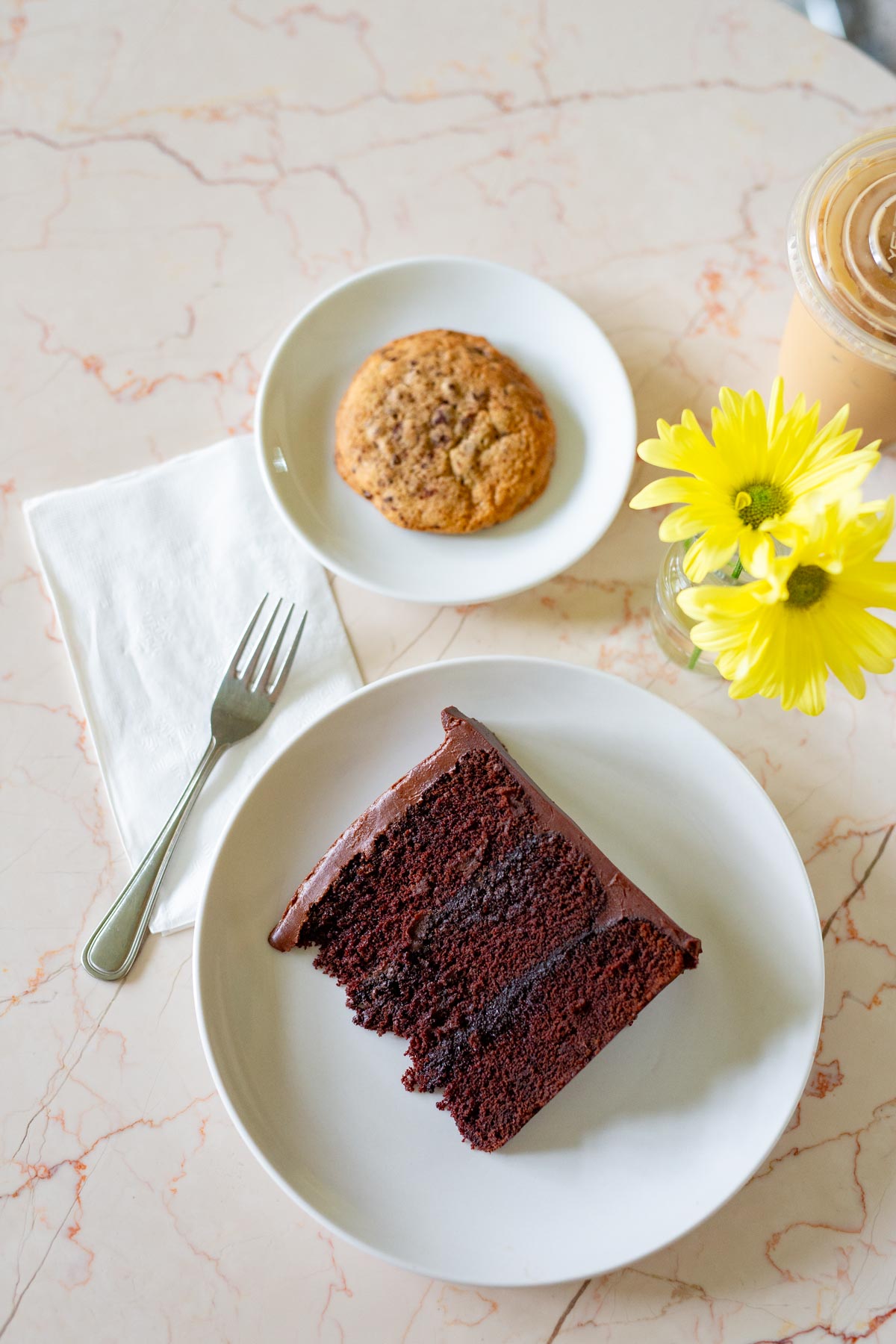 Aerial view of the 3 layer chocolate cake at the Chocolate Room with a cookie, flowers, and coffee in the background, one of the best things to do in Carroll Gardens Brooklyn