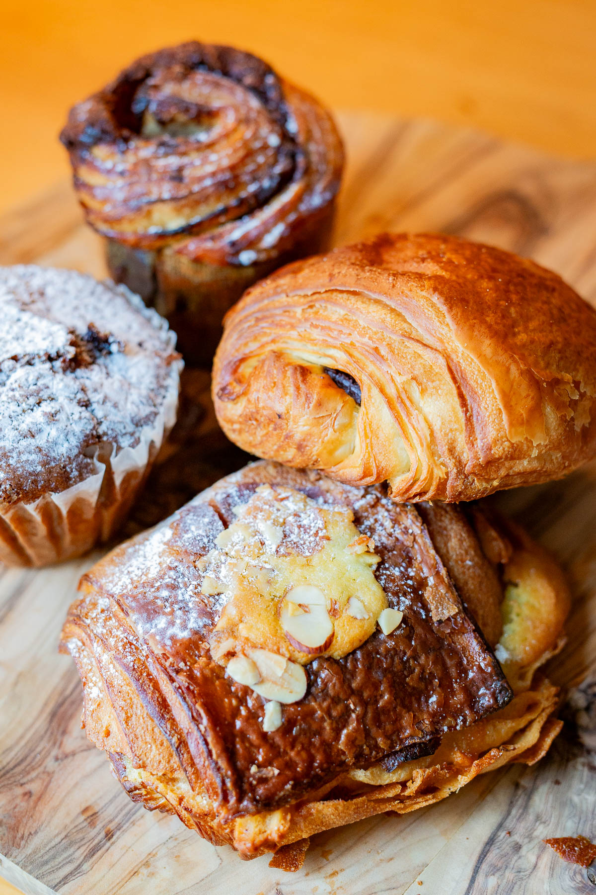 Too Good To Go Order. Chocolate croissant, almond croissant, banana muffin and a Nutella croissant cupcake on a wooden cutting board