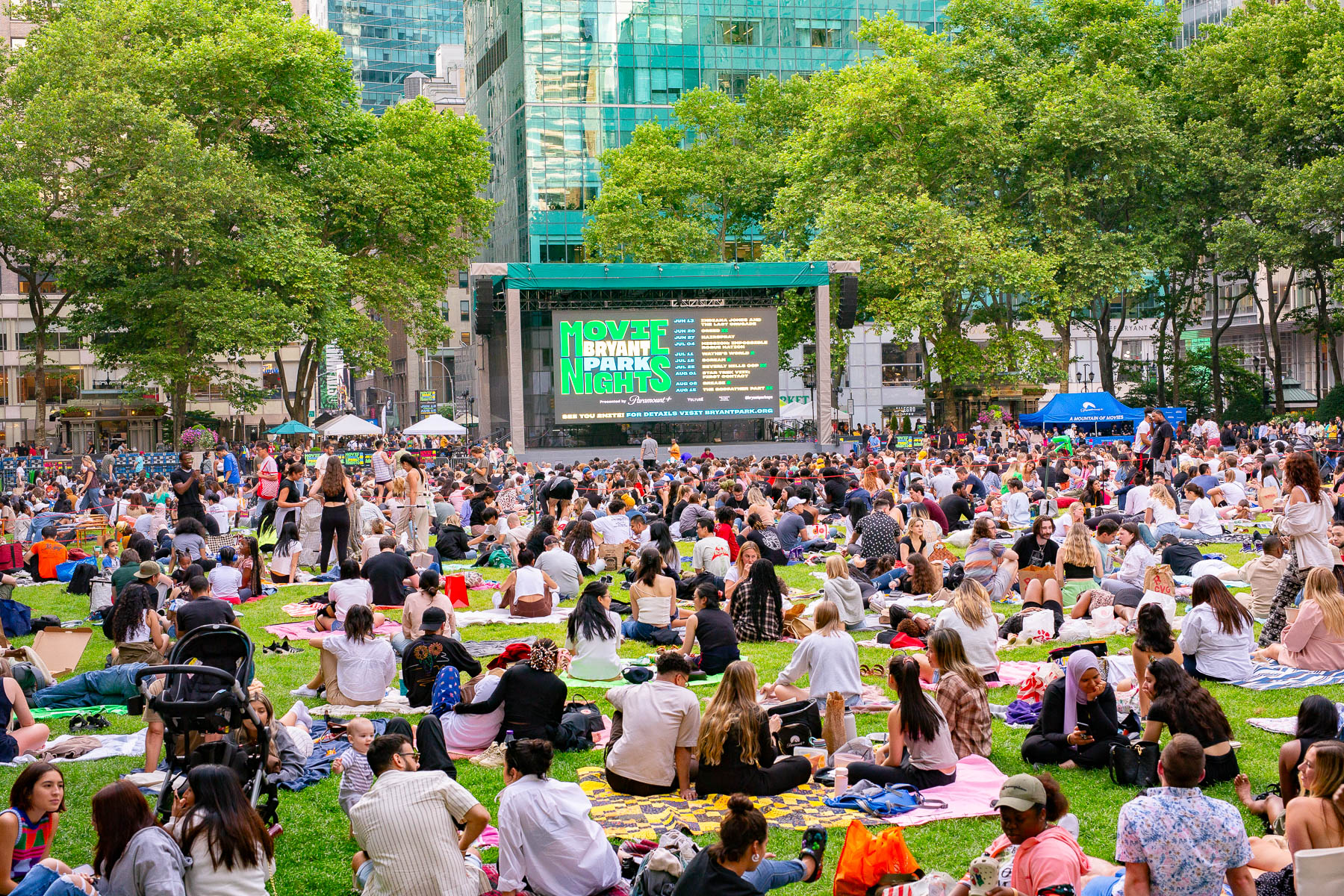 A large crowd sits on blankets on the lawn at Bryant Park watching an outdoor movie screening.