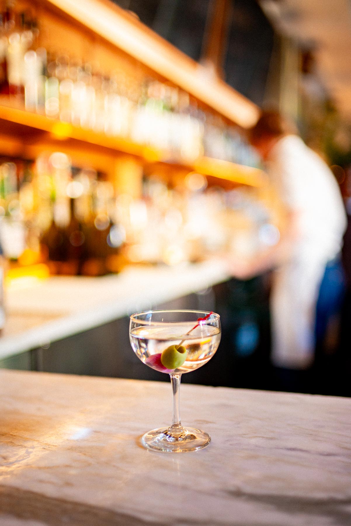 A martini glass with an olive garnish sits on a marble bar counter at Le Crocodile.