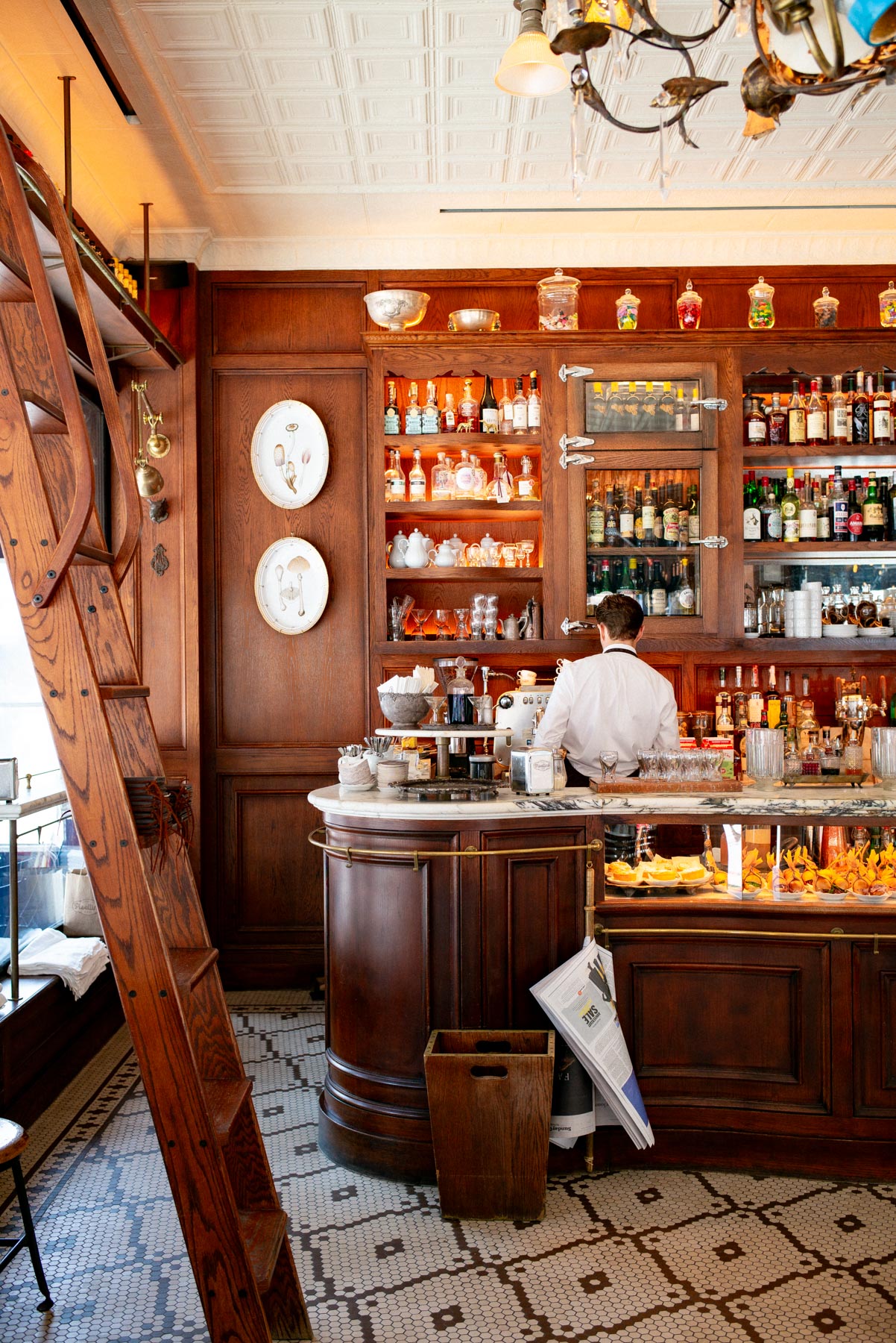 A bartender works behind the wooden bar at an Italian-style café with shelves of bottles.