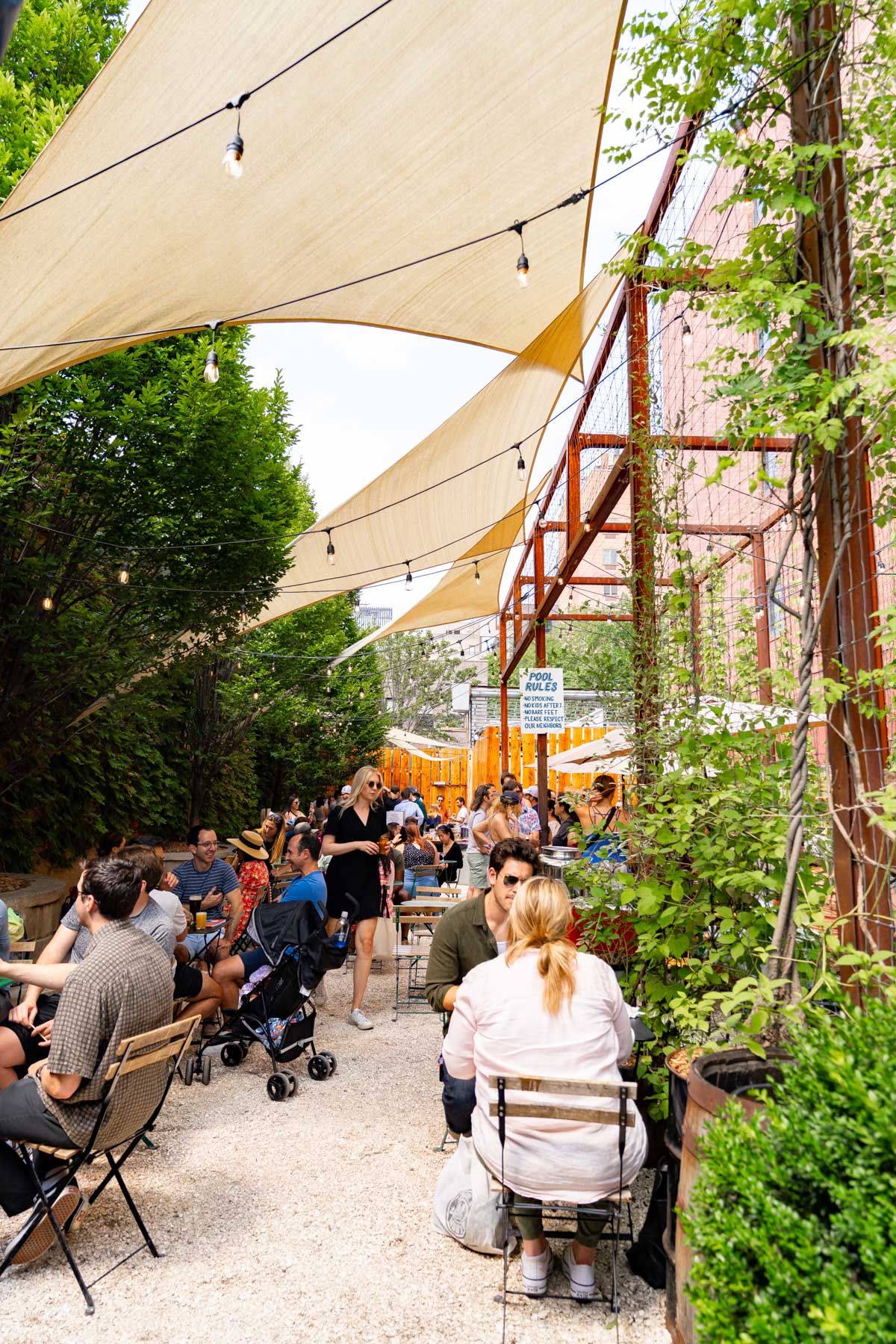 People sit at tables under sail shades in a brewery's outdoor patio.