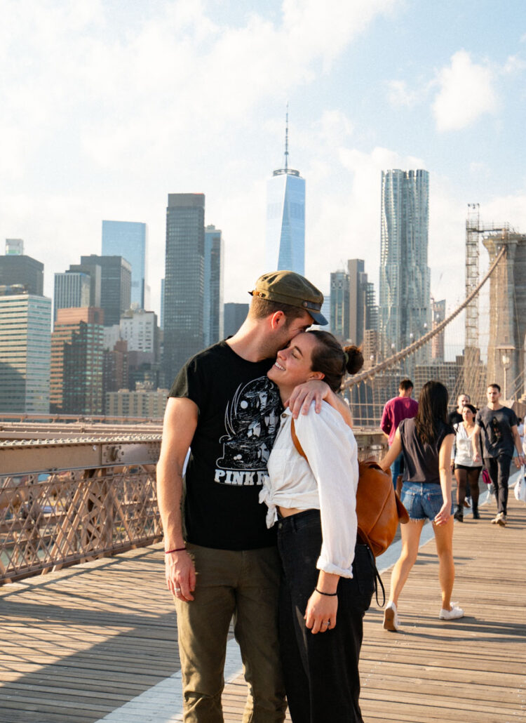 Pedestrians walking across the wood-plank Brooklyn Bridge walkway toward Brooklyn beneath the Gothic stone towers