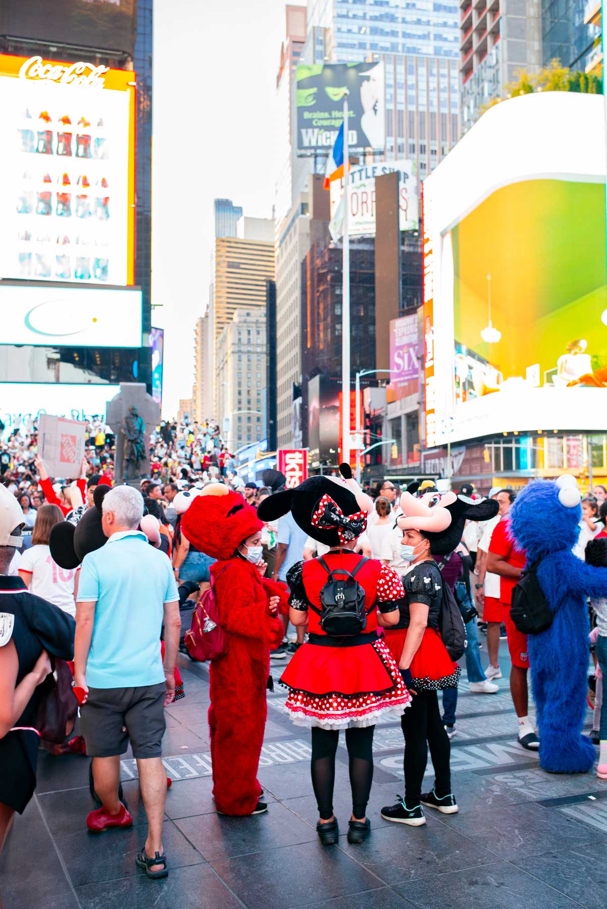 John's Pizzeria of Times Square, costumed characters and crowds fill Times Square beneath billboards.