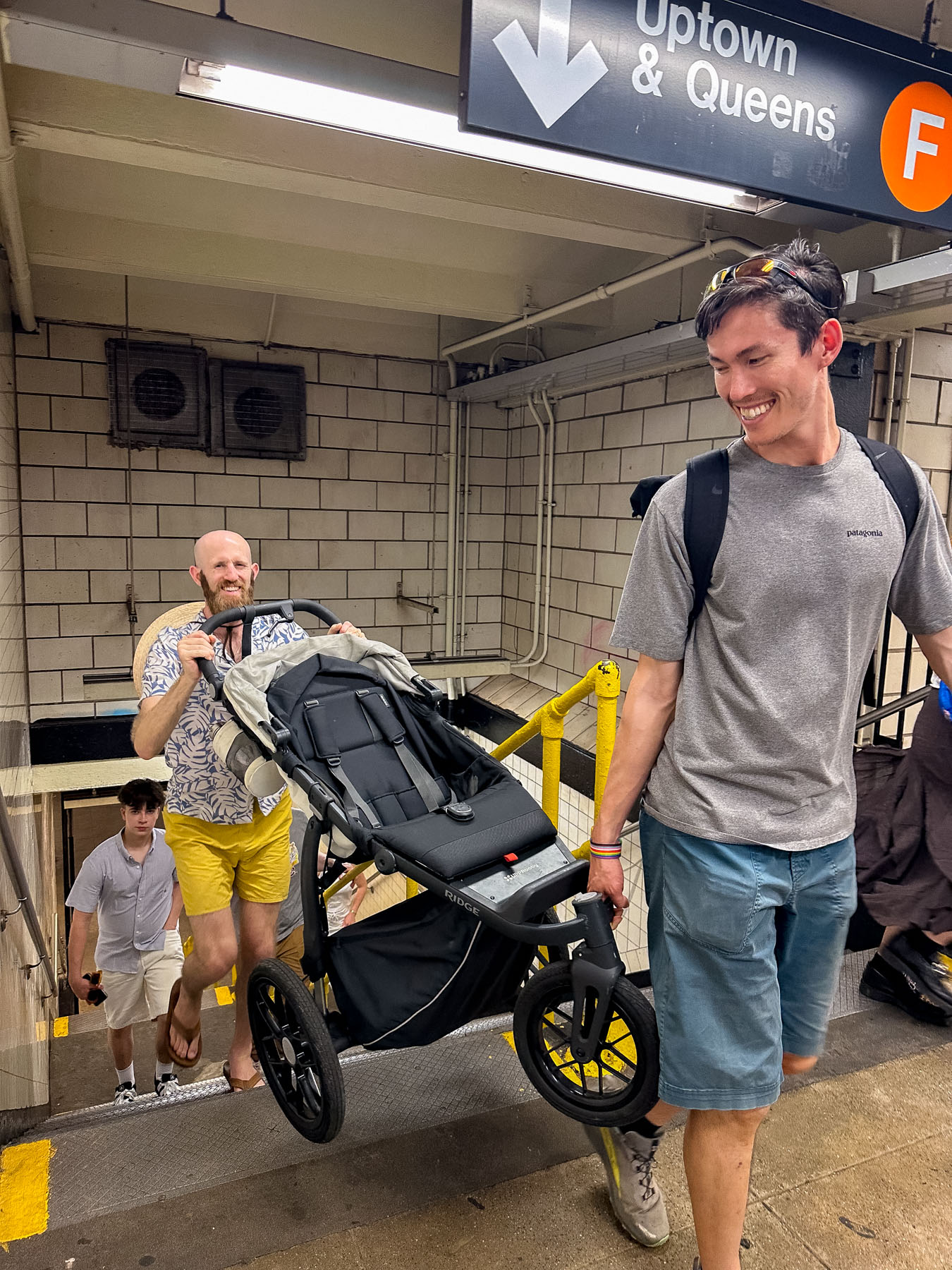 Two men carrying a stroller up subway stairs in New York City
