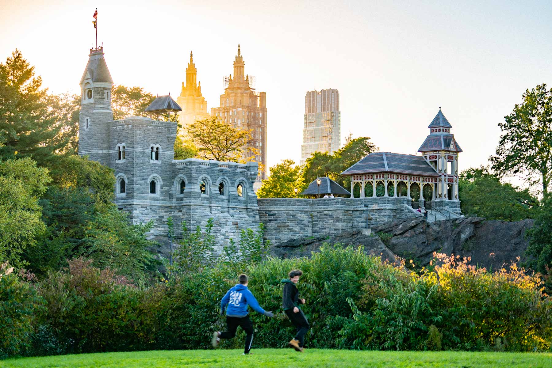 Two boys run across a lawn in front of Belvedere Castle in Central Park at golden hour.